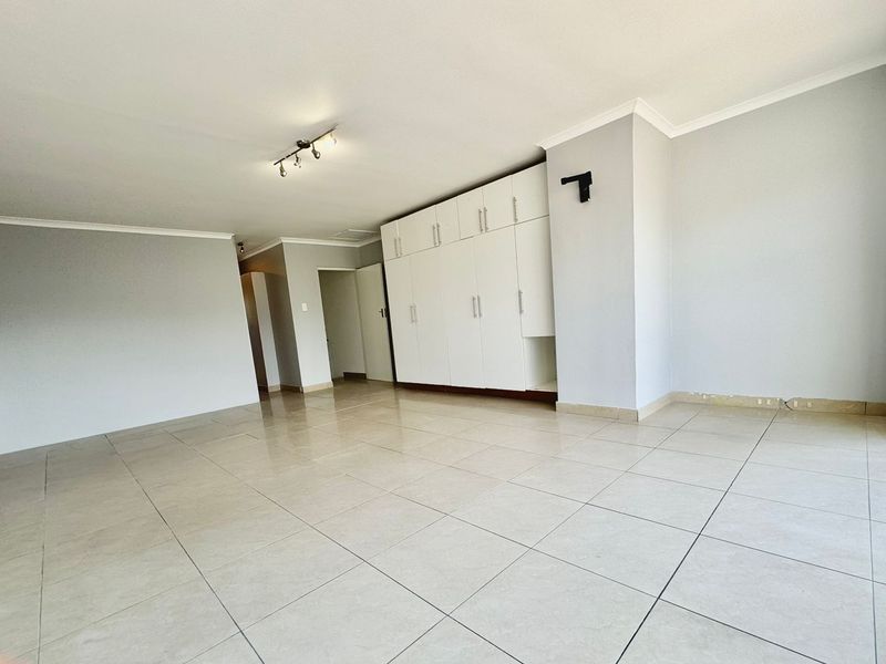 A spacious, empty bedroom featuring neutral tiled flooring, built-in cupboards, and clean white walls, ready for personalization.