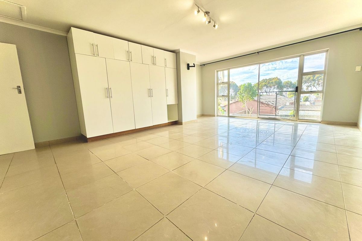 Spacious bedroom featuring large built-in cupboards, polished tiled flooring, and a sliding glass door providing ample natural light.