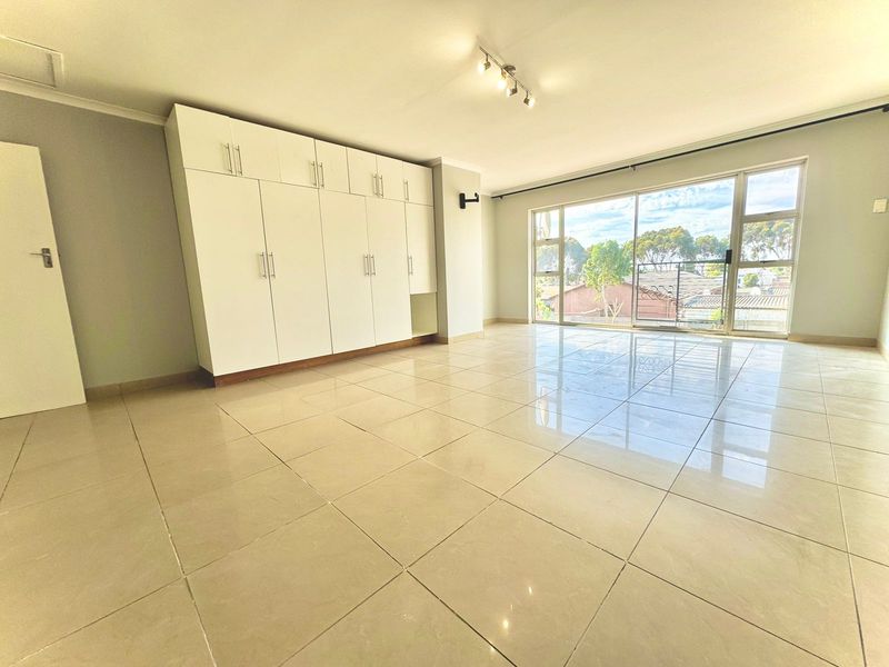 Spacious bedroom featuring large built-in cupboards, polished tiled flooring, and a sliding glass door providing ample natural light.