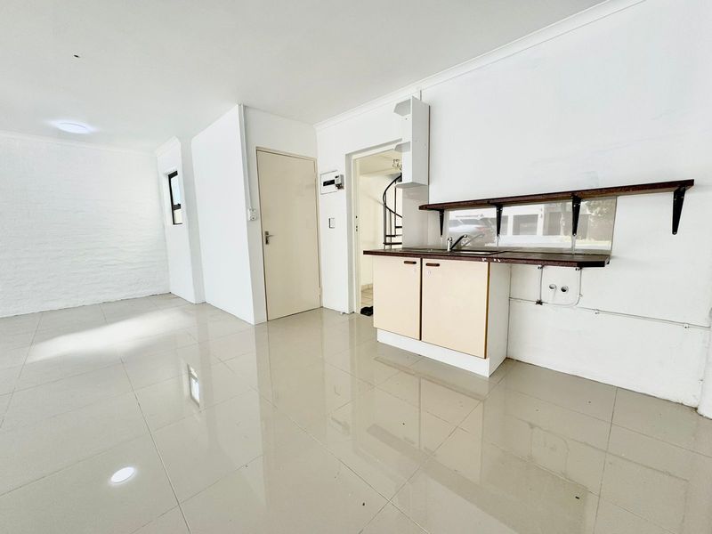 An empty, open-plan kitchen area featuring tiled flooring, basic cabinetry with a sink, and access to a spiral staircase.