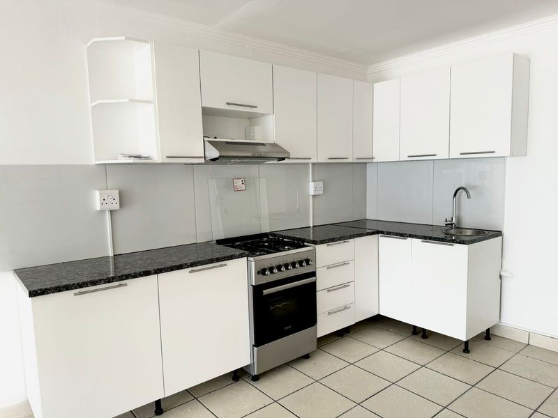 A clean, modern kitchen featuring white cabinetry, granite countertops, a stainless steel gas stove with extractor fan, and tiled flooring.