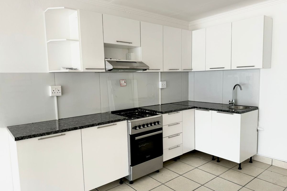 A clean, modern kitchen featuring white cabinetry, granite countertops, a stainless steel gas stove with extractor fan, and tiled flooring.