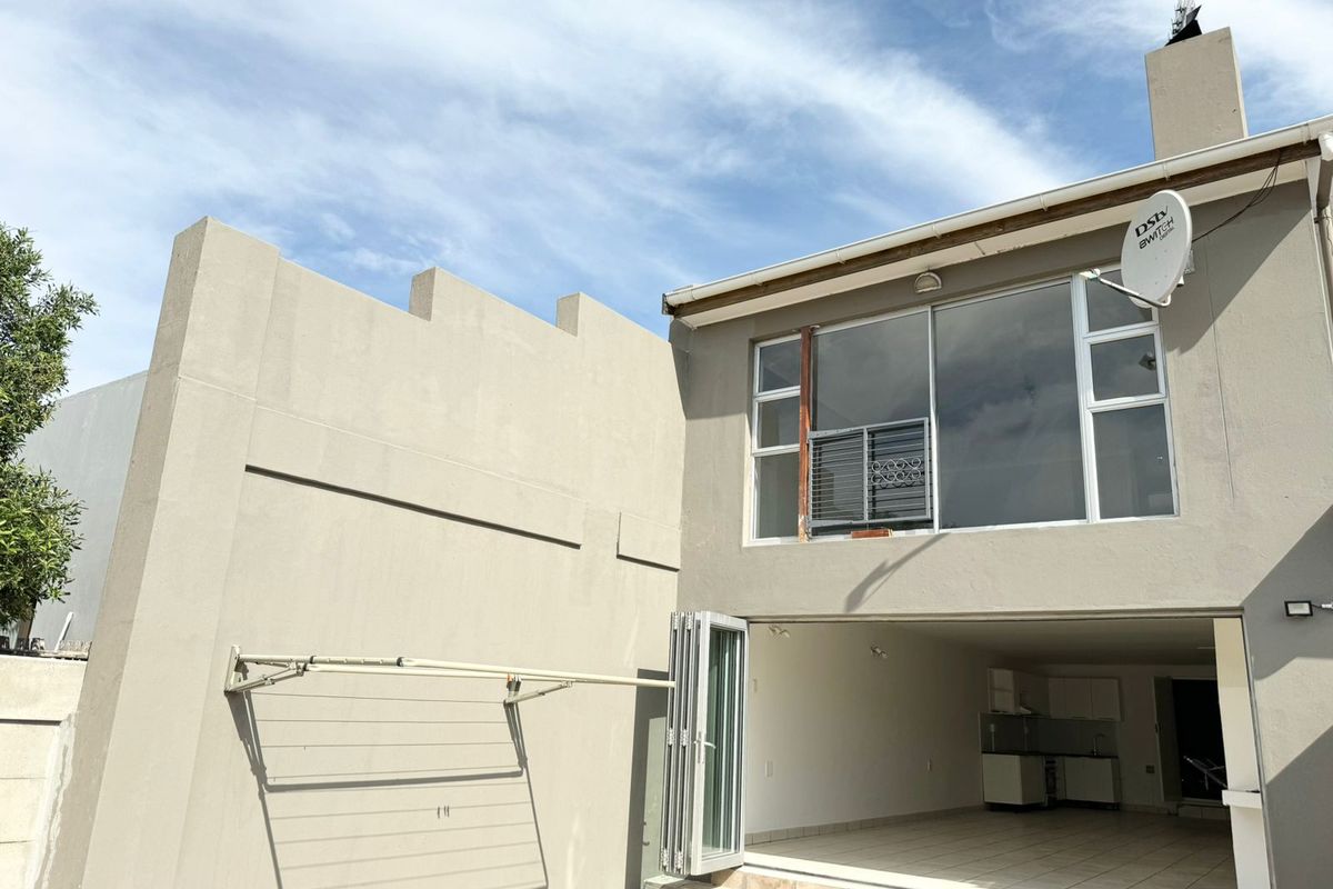 Rear exterior view of the property featuring a tiled patio, folding glass doors, and a wall-mounted drying rack.