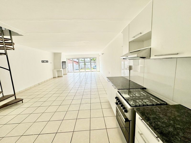 Spacious open-plan living area featuring a modern kitchen with gas stove, tiled flooring, and a spiral staircase leading to an upper level.