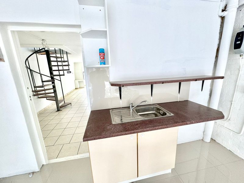 A functional scullery area featuring a stainless steel sink, laminate countertop, and built-in cabinetry, with an adjacent spiral staircase leading to another level.