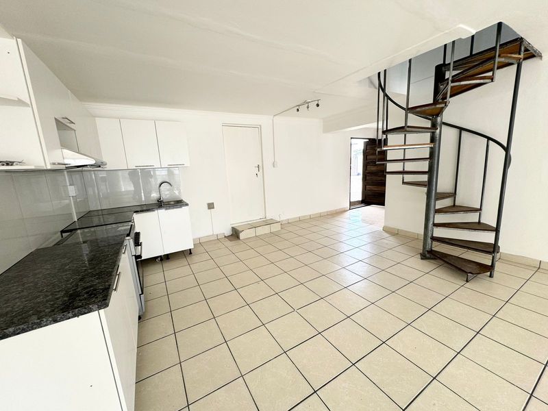 Open-plan kitchen area featuring white cabinetry, granite countertops, and a distinctive spiral staircase leading to the upper level.