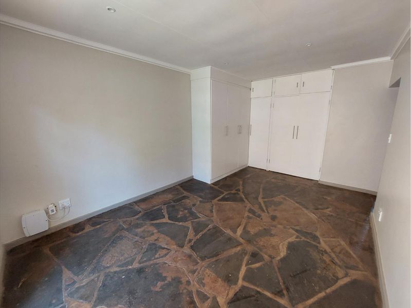 A spacious, empty bedroom featuring unique stone flooring, neutral walls, and ample built-in cupboard storage.