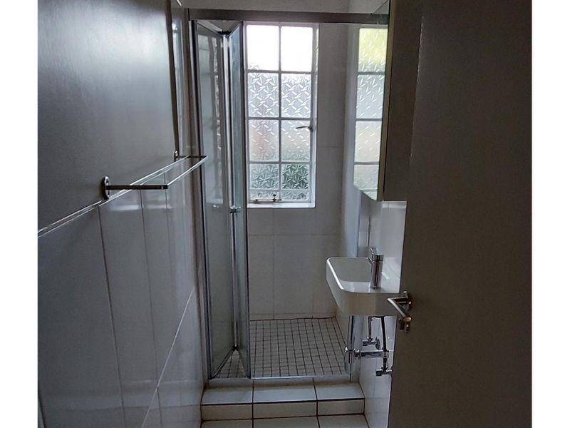 A compact bathroom featuring a shower enclosure, wall-mounted basin, and tiled finishes with an obscured glass window for privacy.