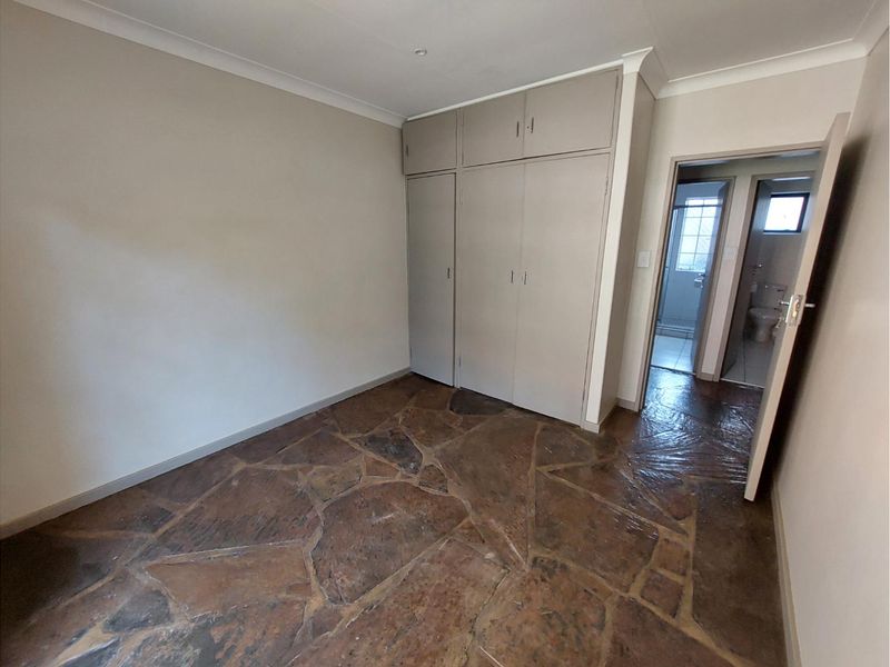 An empty bedroom featuring unique stone flooring, built-in cupboards, and direct access to an adjacent bathroom.
