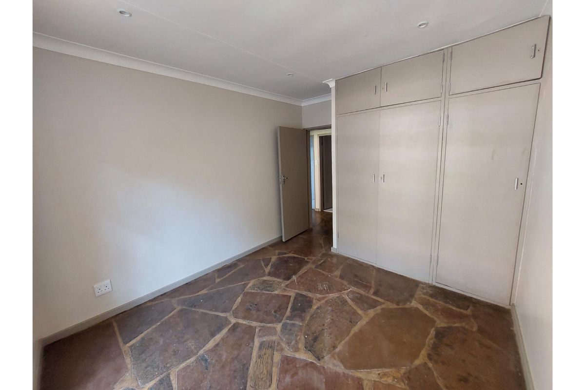 An empty bedroom featuring built-in cupboards, recessed lighting, and distinctive stone flooring, offering a neutral canvas for personalization.