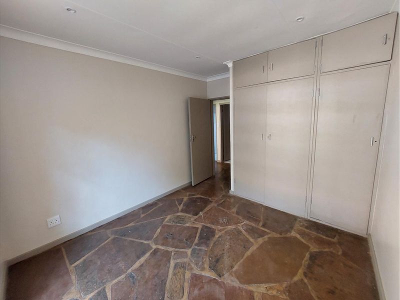 An empty bedroom featuring built-in cupboards, recessed lighting, and distinctive stone flooring, offering a neutral canvas for personalization.