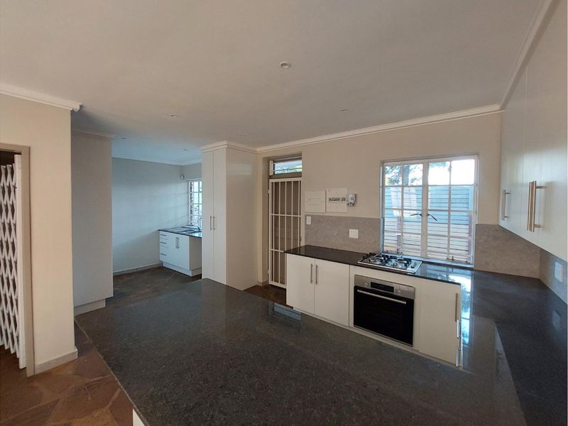Open-plan kitchen featuring granite countertops, built-in oven, gas hob, and ample cabinetry, flowing into a secondary prep area with additional storage.