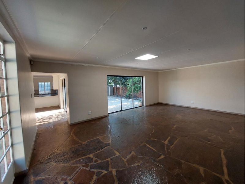 Spacious, empty living area featuring unique flagstone flooring, large sliding glass doors leading to the garden, and a bright skylight.