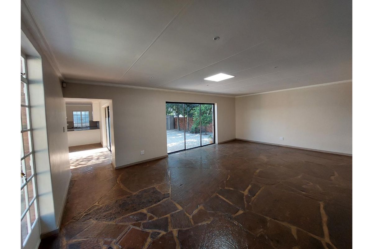 Spacious, empty living area featuring unique flagstone flooring, large sliding glass doors leading to the garden, and a bright skylight.