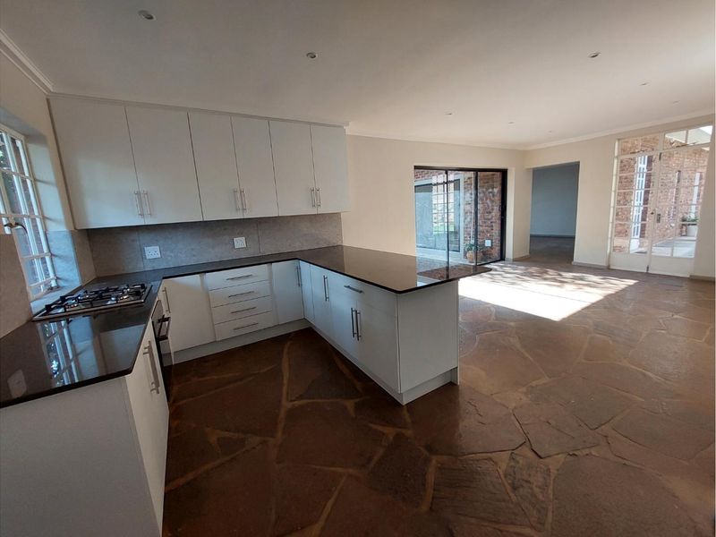 Spacious open-plan kitchen featuring white cabinetry, granite countertops, gas hob, and unique stone flagstone flooring, flowing into an adjacent living area.