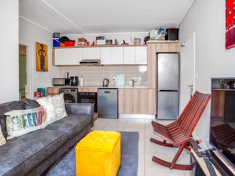 Compact open-plan living area featuring a modern kitchenette with built-in cabinetry, integrated appliances, and tiled flooring throughout.