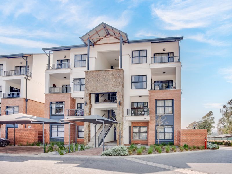 A modern multi-story apartment building featuring a combination of brick and stone facade, private balconies, and covered parking bays.