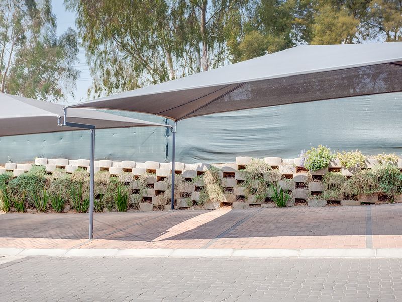 A paved outdoor parking area featuring shade sail structures and a decorative retaining wall with integrated landscaping.