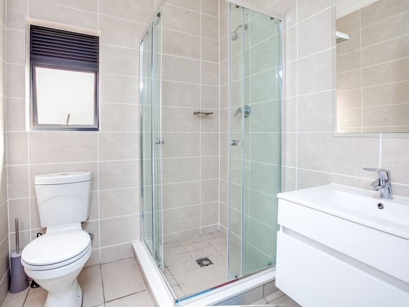 A clean, modern bathroom featuring a glass-enclosed shower, wall-mounted vanity with basin, and neutral floor-to-ceiling tiling.