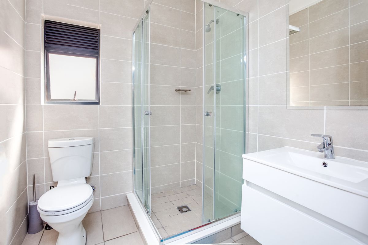A clean, modern bathroom featuring a glass-enclosed shower, wall-mounted vanity with basin, and neutral floor-to-ceiling tiling.