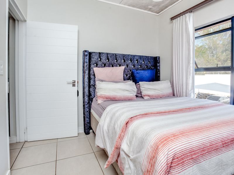 A well-lit bedroom featuring neutral tiled flooring and a large window with an aluminium frame, providing natural light and a view of the exterior.