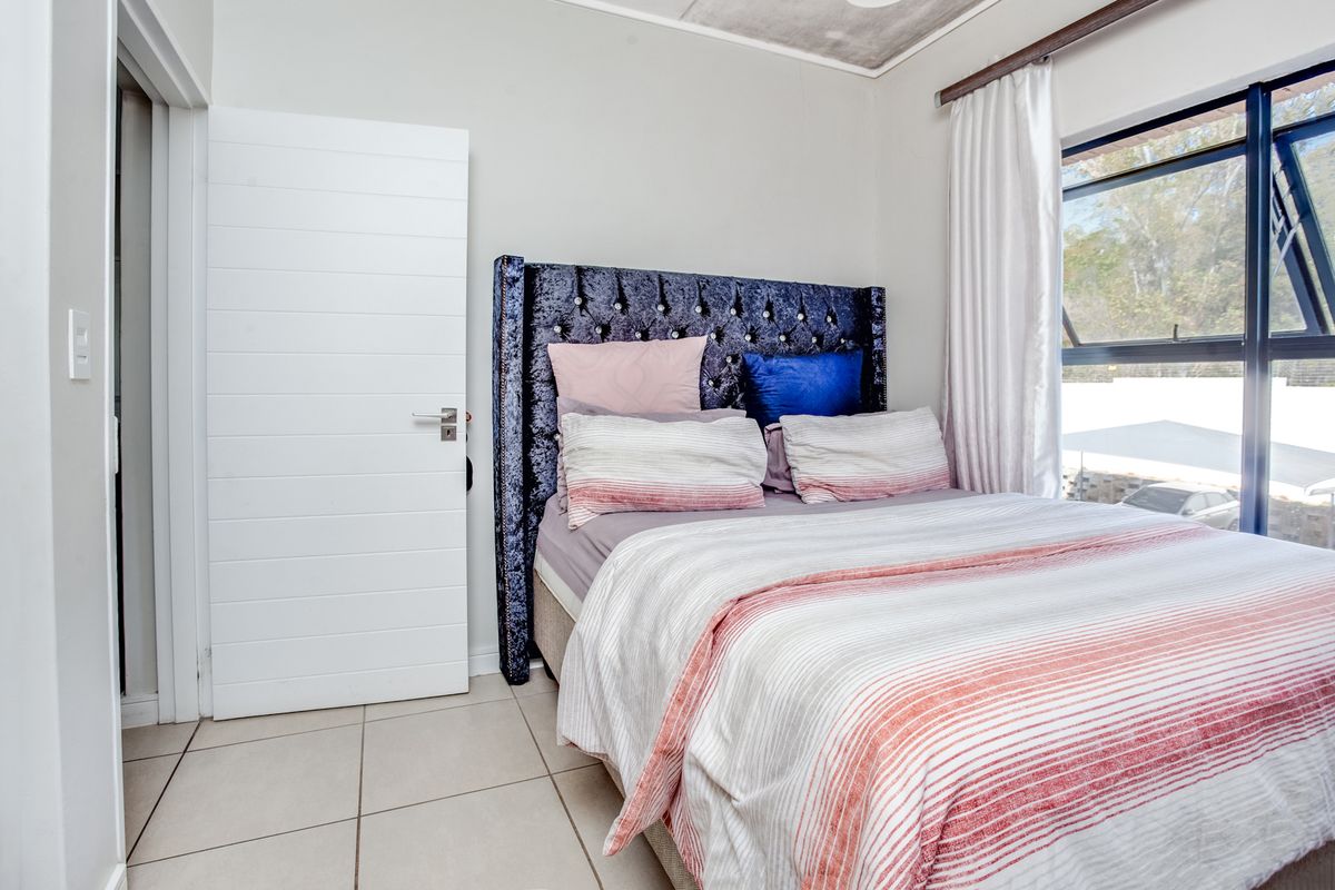 A well-lit bedroom featuring neutral tiled flooring and a large window with an aluminium frame, providing natural light and a view of the exterior.