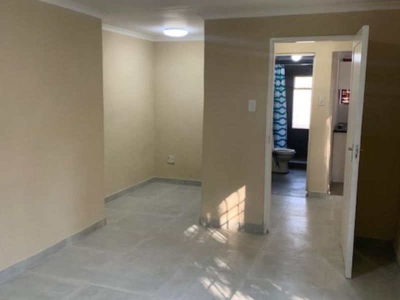 An empty living area featuring neutral walls, tiled flooring, and coved cornicing, with a clear view through to the adjacent bathroom and kitchen area.