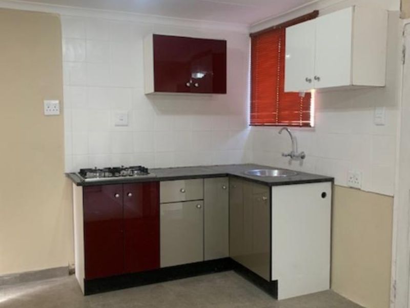 A compact kitchen featuring a gas hob, stainless steel sink, tiled backsplash, and a mix of red and neutral built-in cabinetry.