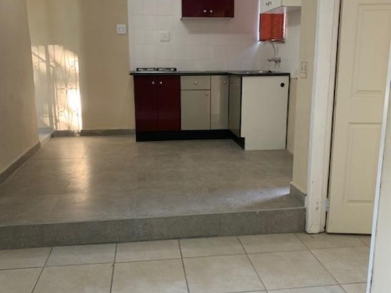 A compact, empty kitchen area featuring built-in cabinetry, a tiled splashback, and a raised floor level, offering a functional space ready for updates.