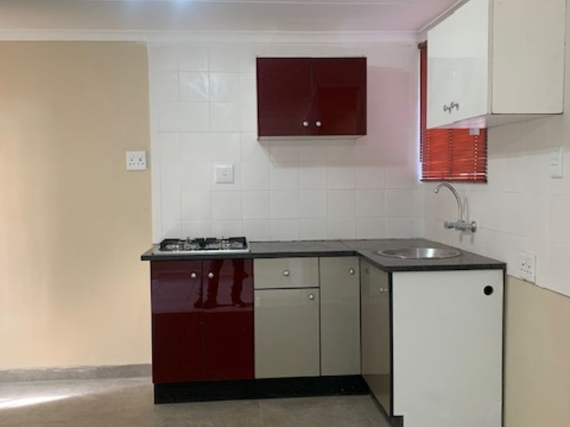 A compact kitchen featuring built-in cabinetry, a gas hob, and a stainless steel sink with tiled splashbacks.