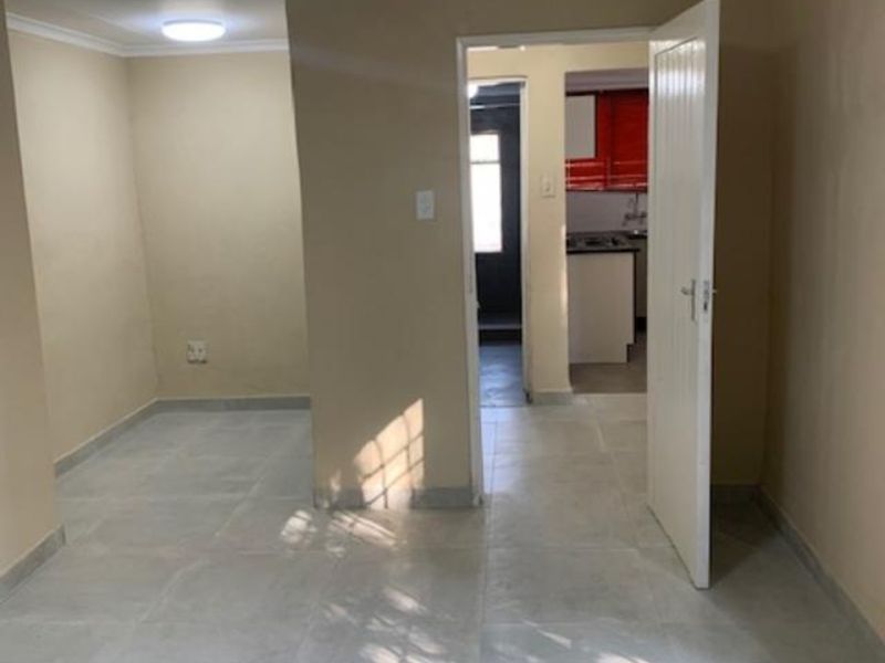 An empty living area featuring neutral wall tones, tiled flooring, and coved ceilings, with a view through to the kitchen area.