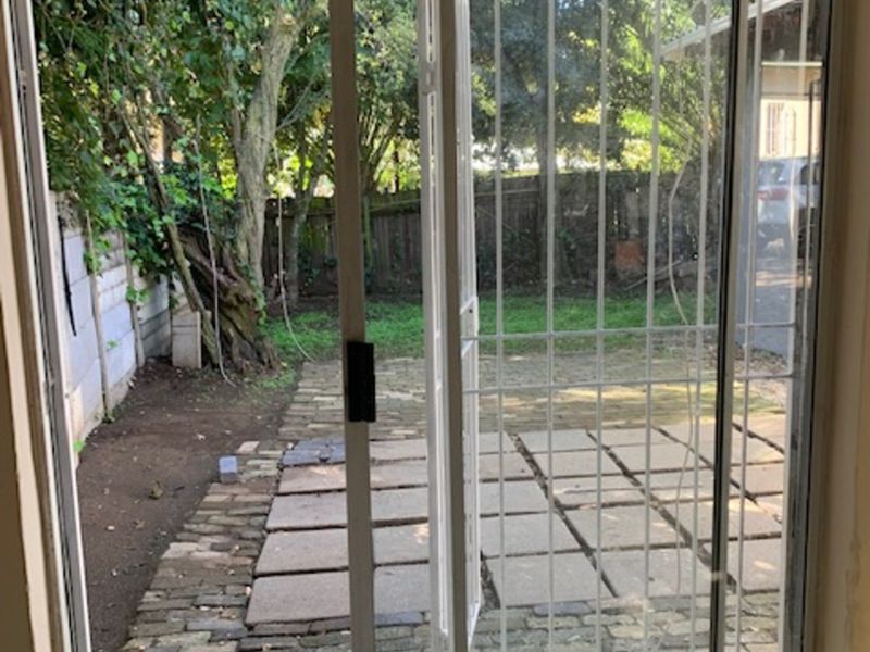 View from an interior space looking out onto a paved patio area with a security gate and garden access.