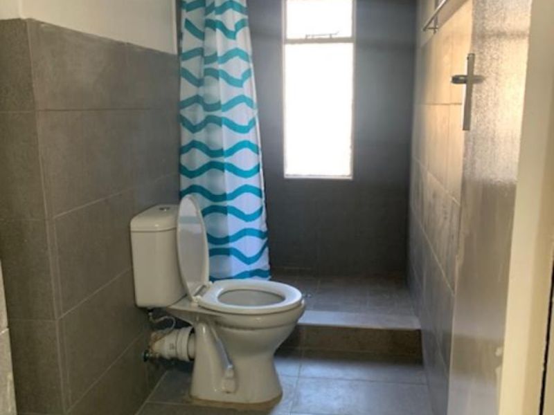 A functional bathroom featuring grey wall and floor tiles, a toilet, and a shower area with a curtain.