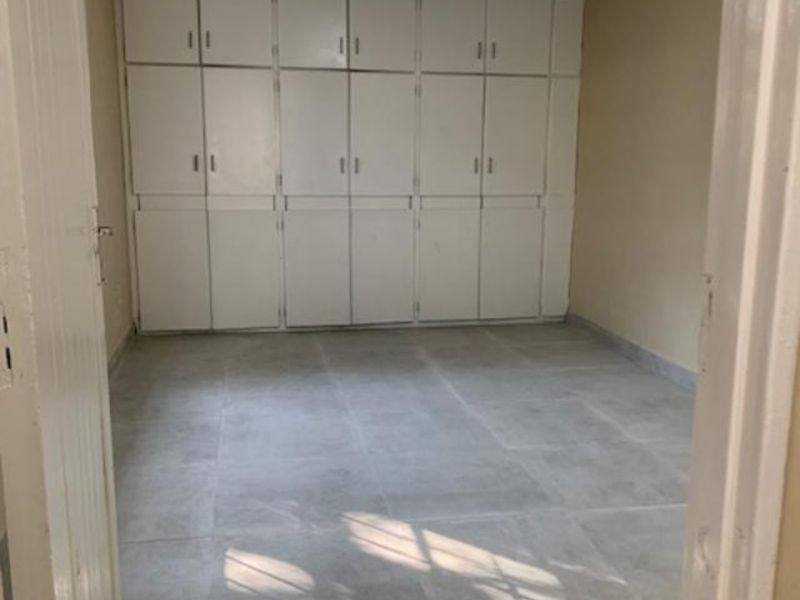 An empty bedroom featuring neutral tiled flooring and extensive floor-to-ceiling built-in cupboards providing ample storage space.