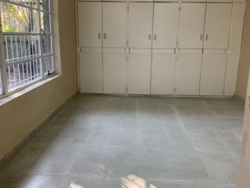 A bright, empty bedroom featuring neutral tiled flooring and extensive floor-to-ceiling built-in storage cupboards.