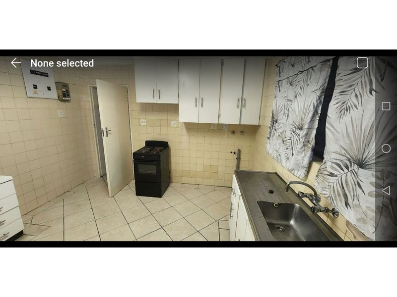 A dated kitchen featuring tiled walls and flooring, built-in cabinetry, a stainless steel sink, and a freestanding stove.