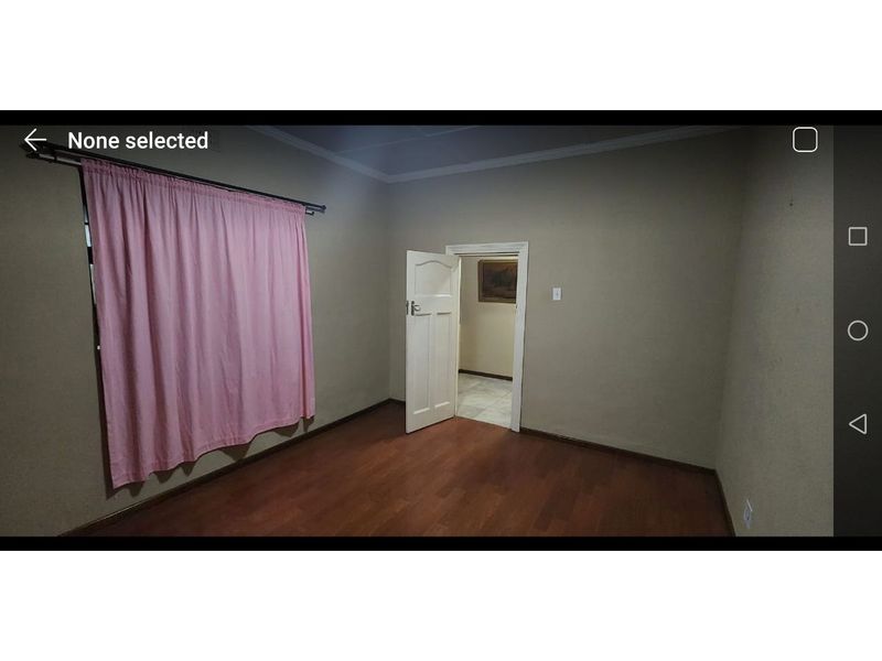 An empty bedroom featuring laminate flooring, neutral wall paint, and a classic timber door leading to an adjacent space.