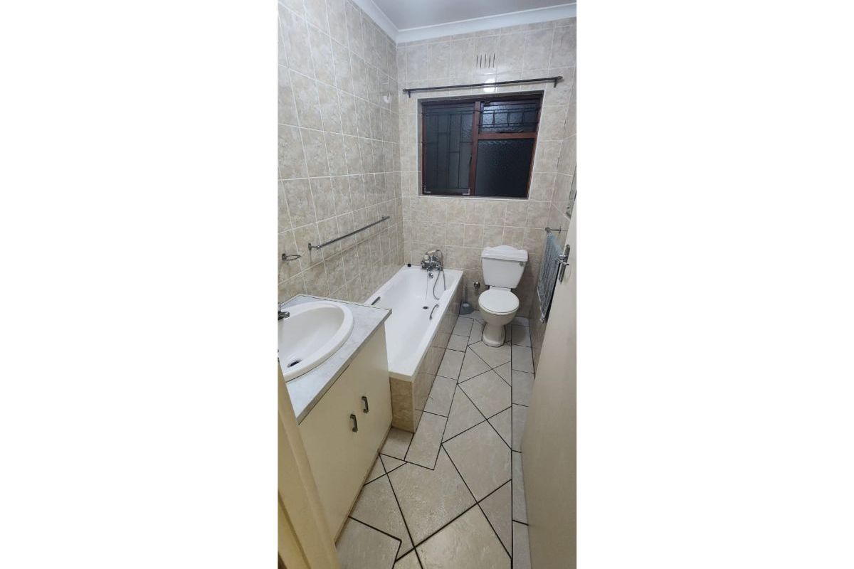 A dated bathroom featuring a bathtub, toilet, and vanity cabinet with tiled walls and flooring, requiring cosmetic updates to improve its overall condition.