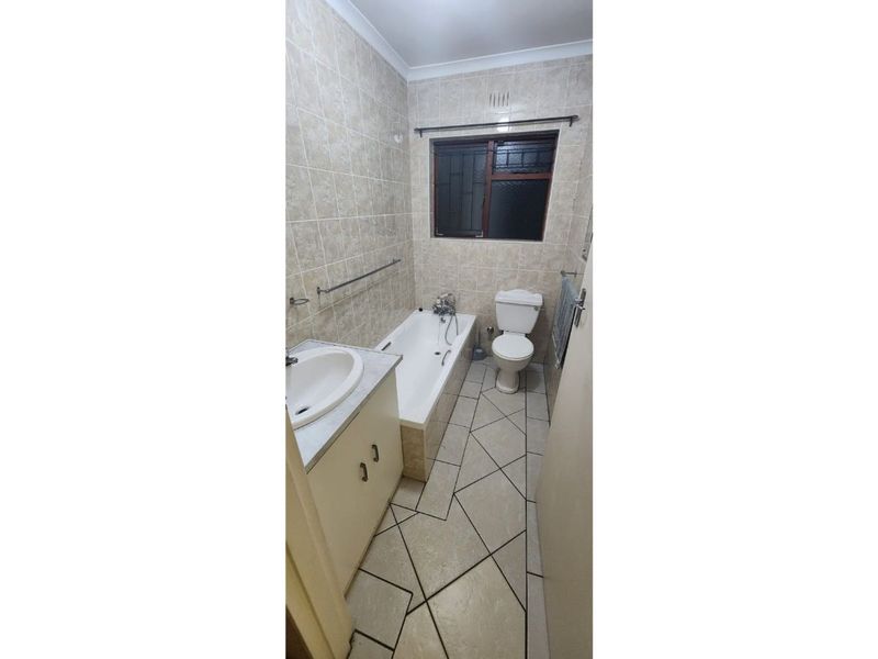 A dated bathroom featuring a bathtub, toilet, and vanity cabinet with tiled walls and flooring, requiring cosmetic updates to improve its overall condition.