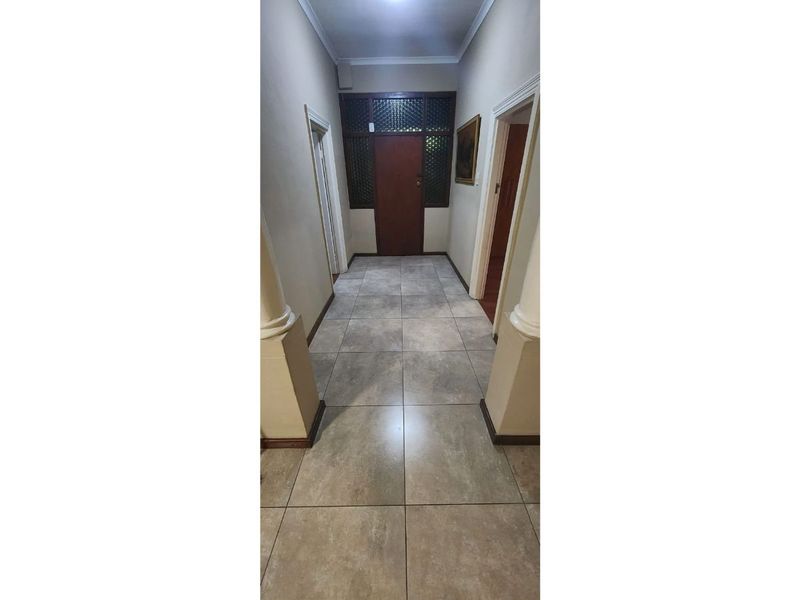 A spacious hallway featuring neutral tiled flooring, decorative columns, and a solid timber front door with a transom window.