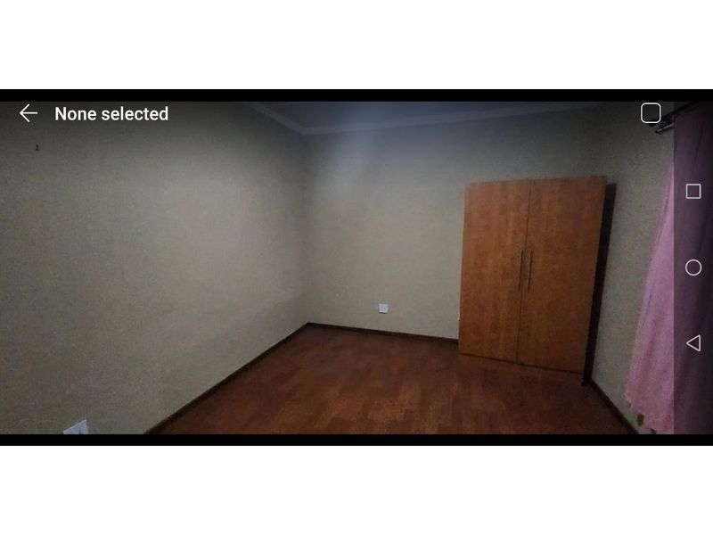 A simple, empty bedroom featuring laminate flooring and a built-in wooden wardrobe.