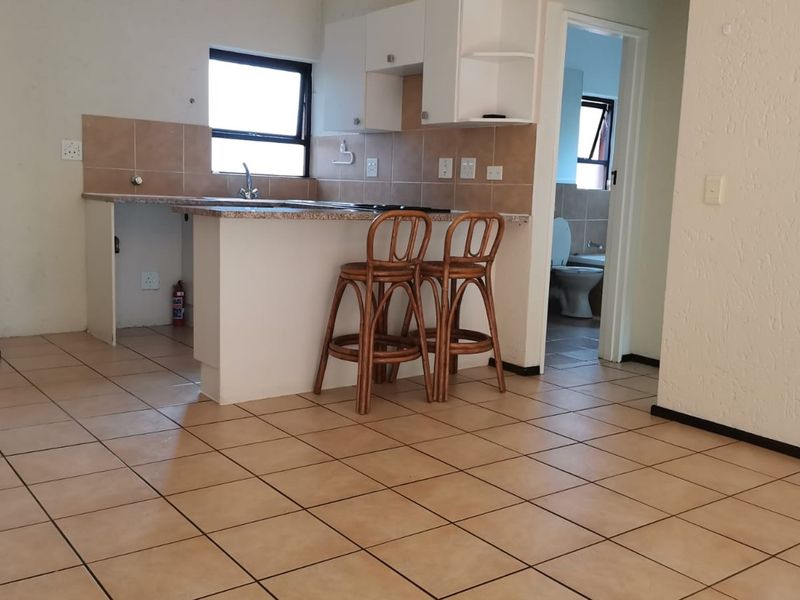 Open plan living area featuring a functional kitchen with granite countertops, tiled backsplash, and a breakfast bar, with direct access to the bathroom.