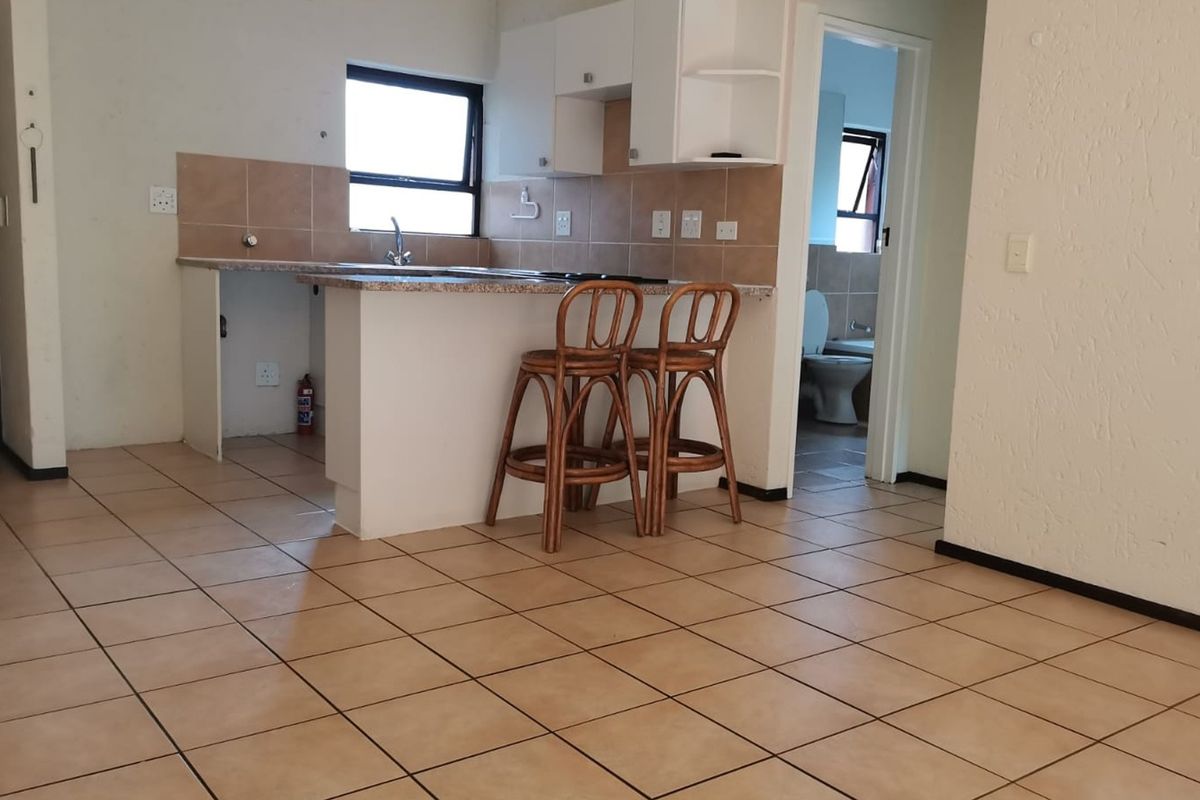 Open plan living area featuring a functional kitchen with granite countertops, tiled backsplash, and a breakfast bar, with direct access to the bathroom.