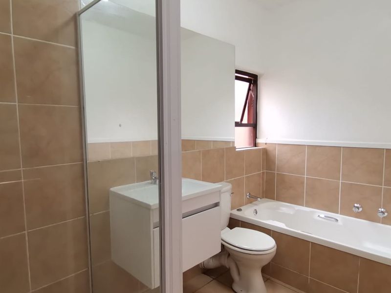 A functional bathroom featuring a built-in vanity, bathtub, shower enclosure, and neutral wall tiling.