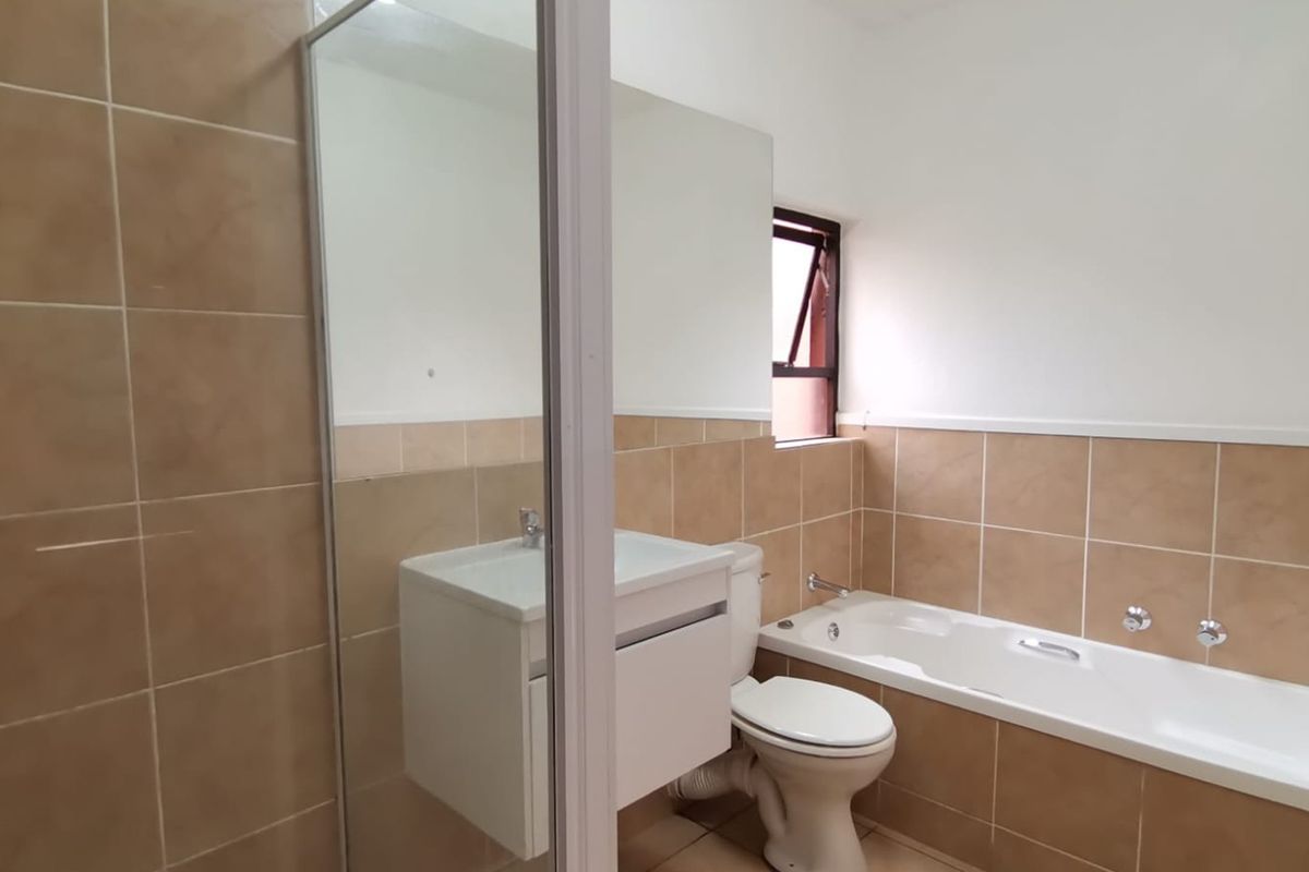 A functional bathroom featuring a built-in vanity, bathtub, shower enclosure, and neutral wall tiling.