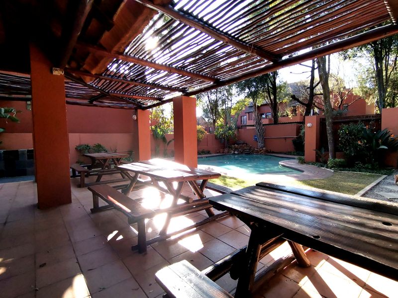 Outdoor entertainment area featuring a swimming pool, paved patio, and a covered thatched pergola structure.