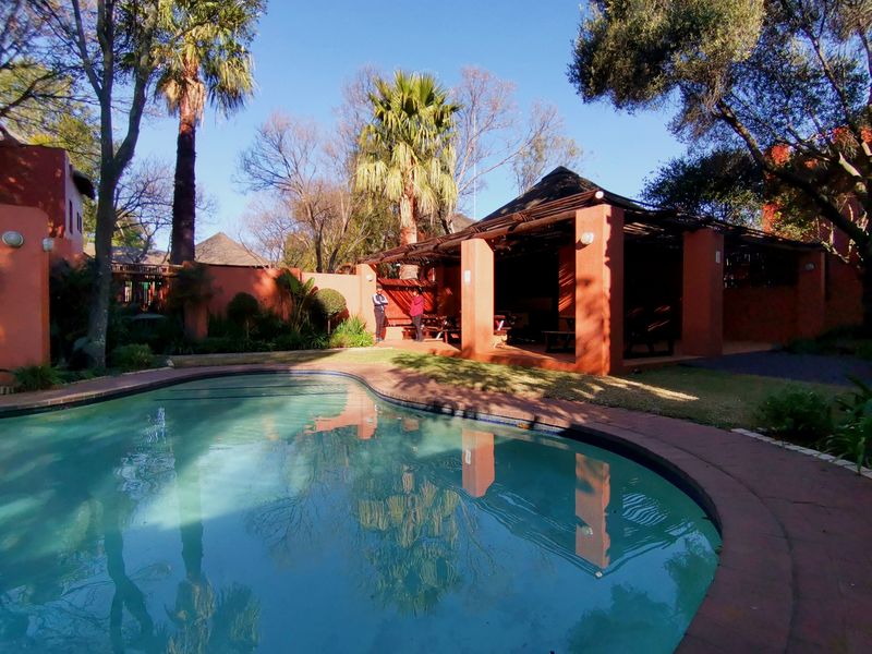 Outdoor pool area featuring a swimming pool, brick paving, and a covered thatched gazebo structure within a landscaped garden setting.