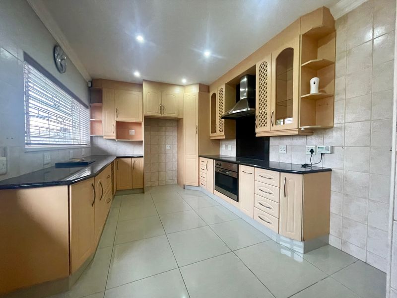A functional kitchen featuring light wood cabinetry, granite countertops, built-in oven, extractor fan, and neutral tiled flooring throughout.