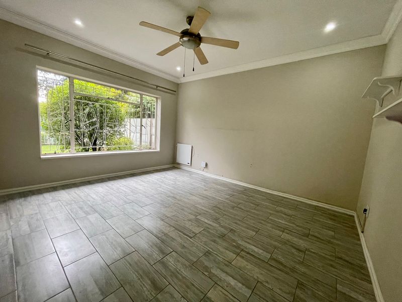 A bright, empty bedroom featuring modern wood-look tiled flooring, a ceiling fan, recessed lighting, and a wall-mounted heater.