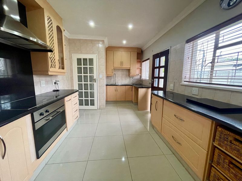 A well-maintained kitchen featuring light wood cabinetry, dark granite countertops, integrated stainless steel appliances, and neutral ceramic floor tiling.